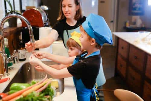 A mom and two kids washing vegetables in the kitchen sink